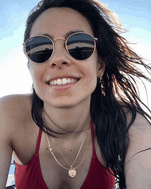 a woman wearing sunglasses and a necklace smiles for the camera