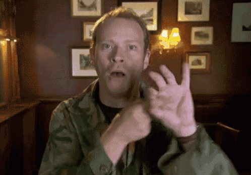 a man in a camouflage shirt is making a funny face with his hands