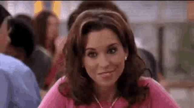 a woman in a pink shirt is sitting at a table in a crowded room .