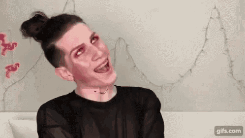 a man wearing makeup and a bun is laughing .