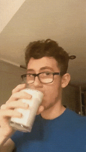 a young man wearing glasses is drinking a glass of milk from a clear glass