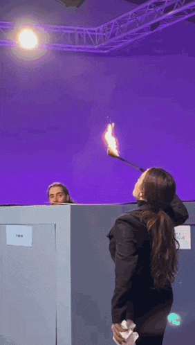 a woman in a black jacket is holding a torch in front of a purple background
