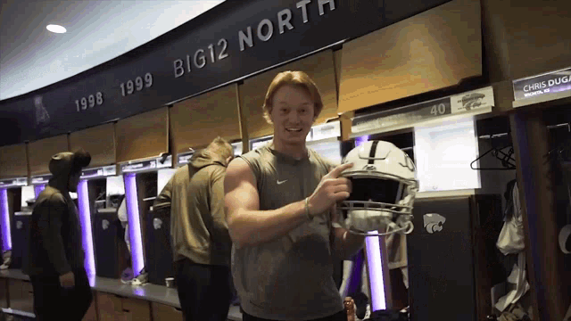 a man holds a football helmet in front of a sign that says big 12 north
