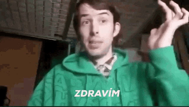 a man in a green hoodie is making a funny face and says zdravím .