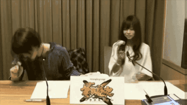 a man and a woman are sitting at a table with microphones and a sign that says emergency on it
