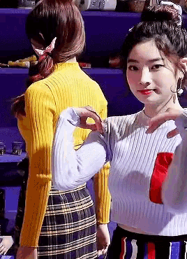 a woman in a yellow sweater is making a heart with her hands