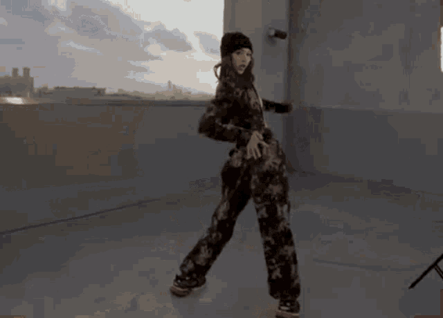 a woman is dancing on a rooftop wearing a camouflage jacket and a beanie .