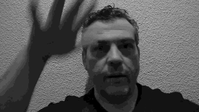 a man in a black shirt is standing in front of a wall with his hands up in the air .