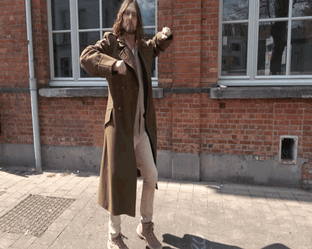 a man in a long coat is standing in front of a brick wall