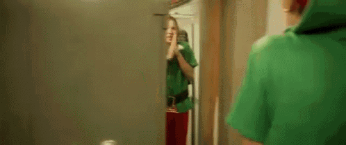 a man in a green elf costume is taking a picture of himself in the mirror .
