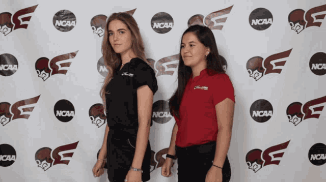 two women standing in front of a ncaa logo