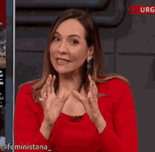 a woman in a red top is clapping her hands in front of a sign that says urg
