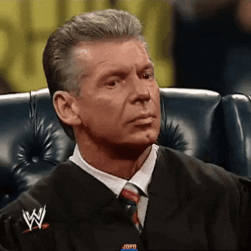 a man in a suit and tie is sitting in a chair with a wwe logo on his jacket .