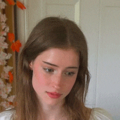 a close up of a woman 's face with flowers on the wall behind her