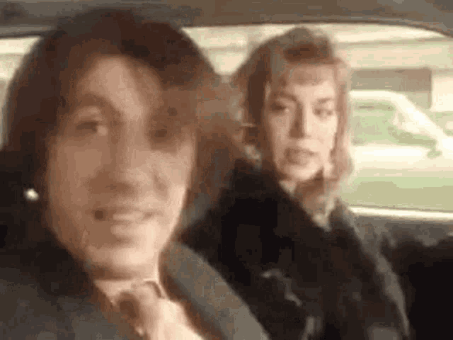a man and a woman are sitting in the back seat of a car and smiling .