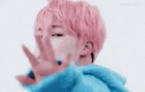 a close up of a person with pink hair making a stop sign with their hand .