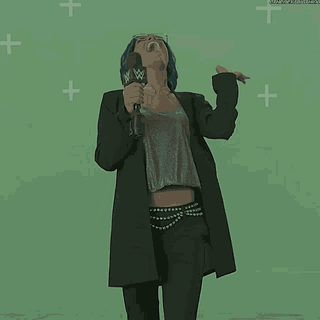 a woman with blue hair is holding a microphone and laughing while standing in front of a green screen .
