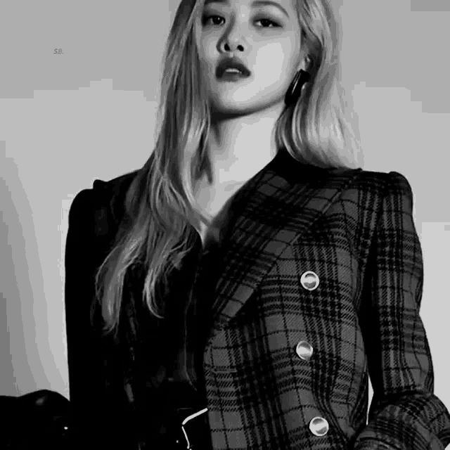 a black and white photo of a woman wearing a plaid jacket and earrings