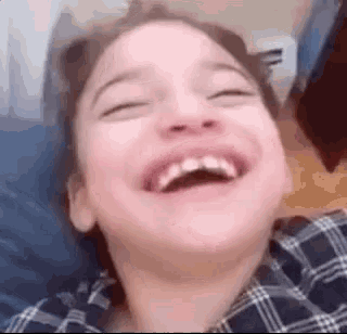 a young girl is laughing with her eyes closed while laying on a bed .