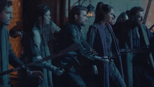 a group of people are standing next to each other holding swords in a dark room .