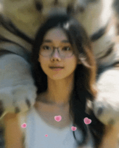 a woman wearing glasses looks at the camera with hearts flying around her