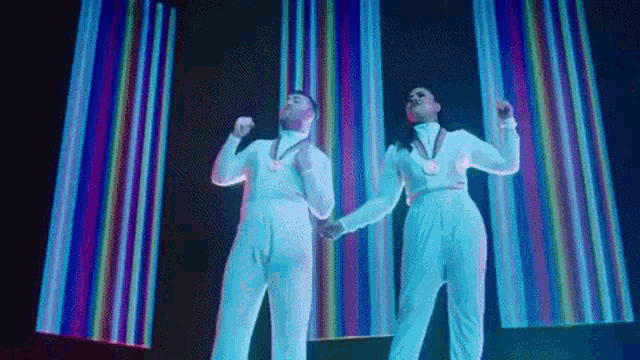 a man and a woman in white jumpsuits are dancing in front of a colorful background .