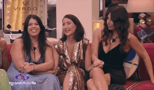 three women are sitting on a couch in front of a sign that says virgo on it