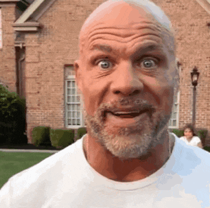 a bald man with a beard is standing in front of a brick house .