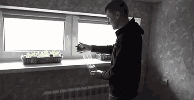 a man is standing on a window sill watering plants