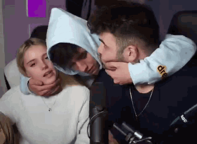 a group of people are hugging each other in front of a microphone while a man holds a woman 's face .