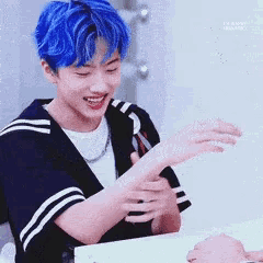 a young man with blue hair is sitting at a table and smiling .