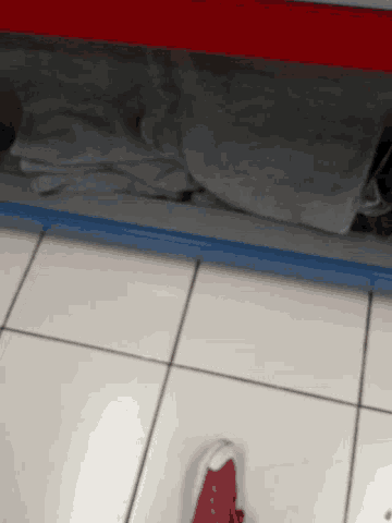 a person standing on a tiled floor with a red shoe