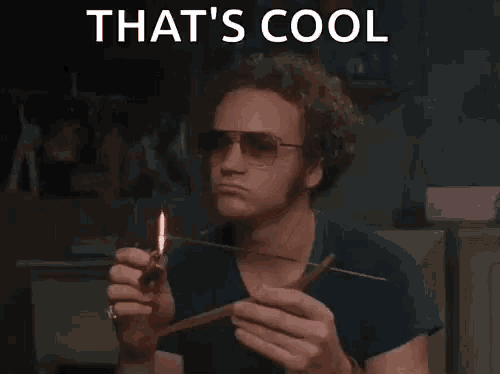 a man wearing sunglasses is lighting a stick with a lighter and the words that 's cool above him .