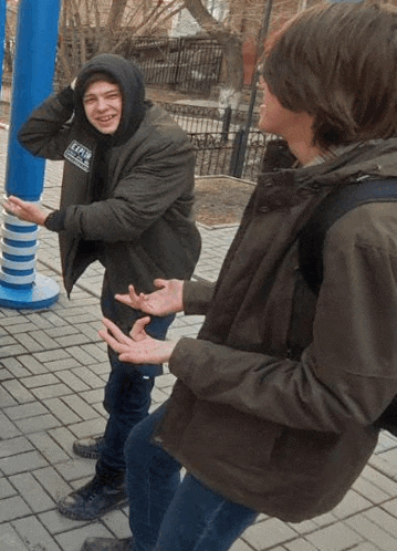 two young men are standing next to each other on a sidewalk . one of the men is wearing a hoodie .
