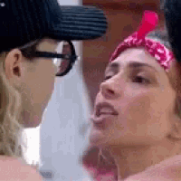 a close up of two women looking at each other . one of the women is wearing glasses and a bandana .