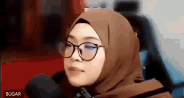 a woman wearing a hijab and glasses is sitting in a car .