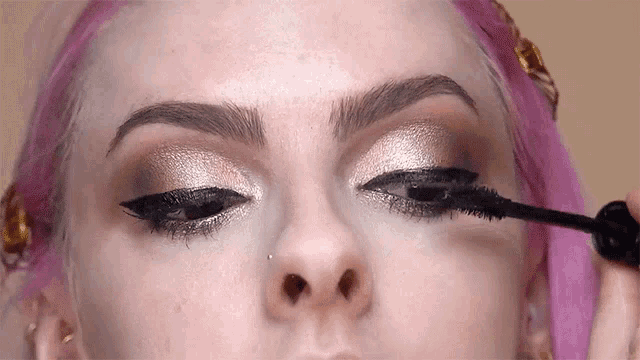 a woman with pink hair applying mascara to her eye