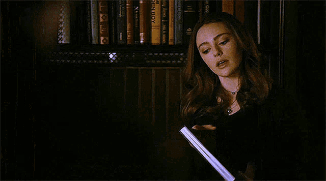 a woman is holding a book in front of a bookshelf in a library .