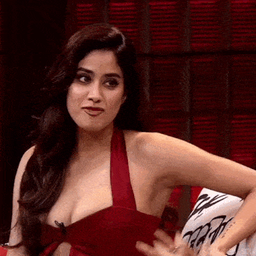 a woman in a red dress is sitting on a couch with her hand on her breast .