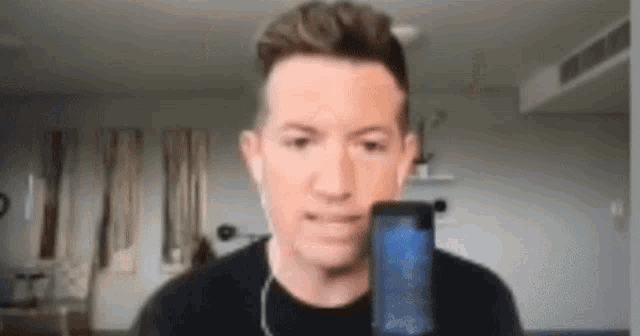 a man wearing headphones is holding a cell phone in front of him .