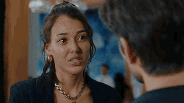 a woman wearing a necklace looks at a man