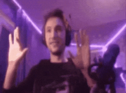 a man wearing headphones is waving his hand in front of a purple light .