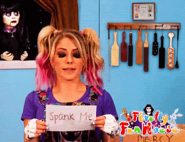 a woman with pink hair holds a sign that says spank me