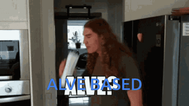 a man with long red hair is standing in a kitchen with the words alive based above him