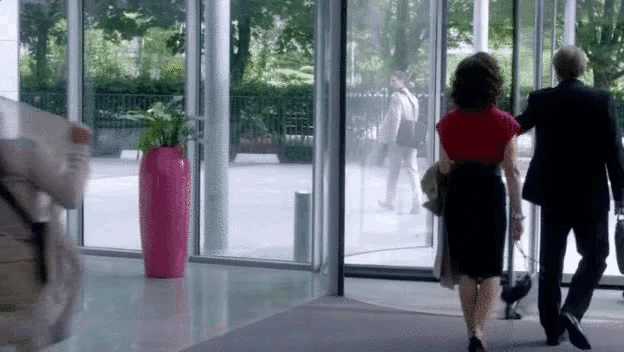a man and a woman are walking out of a building through a glass door .