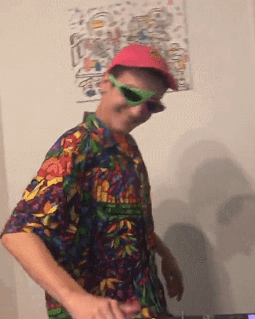 a man wearing sunglasses and a colorful shirt is standing in front of a wall with a drawing on it