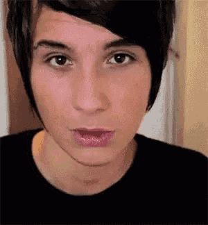 a close up of a young man 's face with a black shirt on and a pink lip .