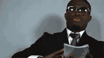 a man in a suit and tie is sitting at a desk holding a piece of paper .