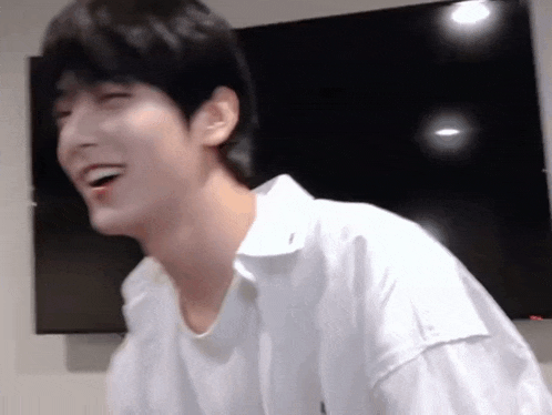 a man in a white shirt is laughing in front of a tv .