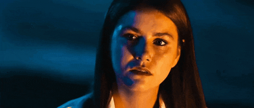 a close up of a woman 's face in a dark room with a blue light behind her .